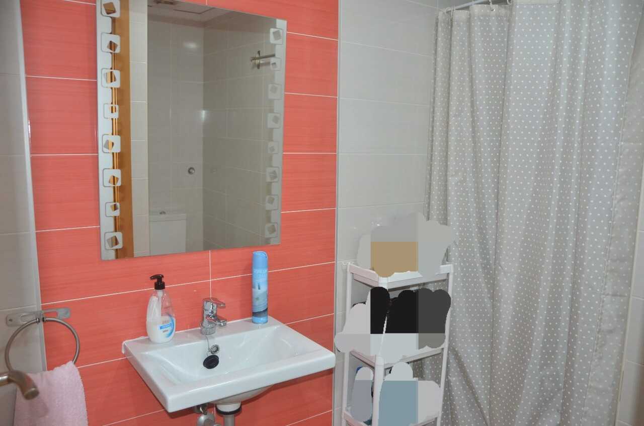 Badezimmer mit korallenfarbenen Wandfliesen, weißem Keramikwaschbecken und dekorativem Spiegel neben einem gepunkteten Duschvorhang.