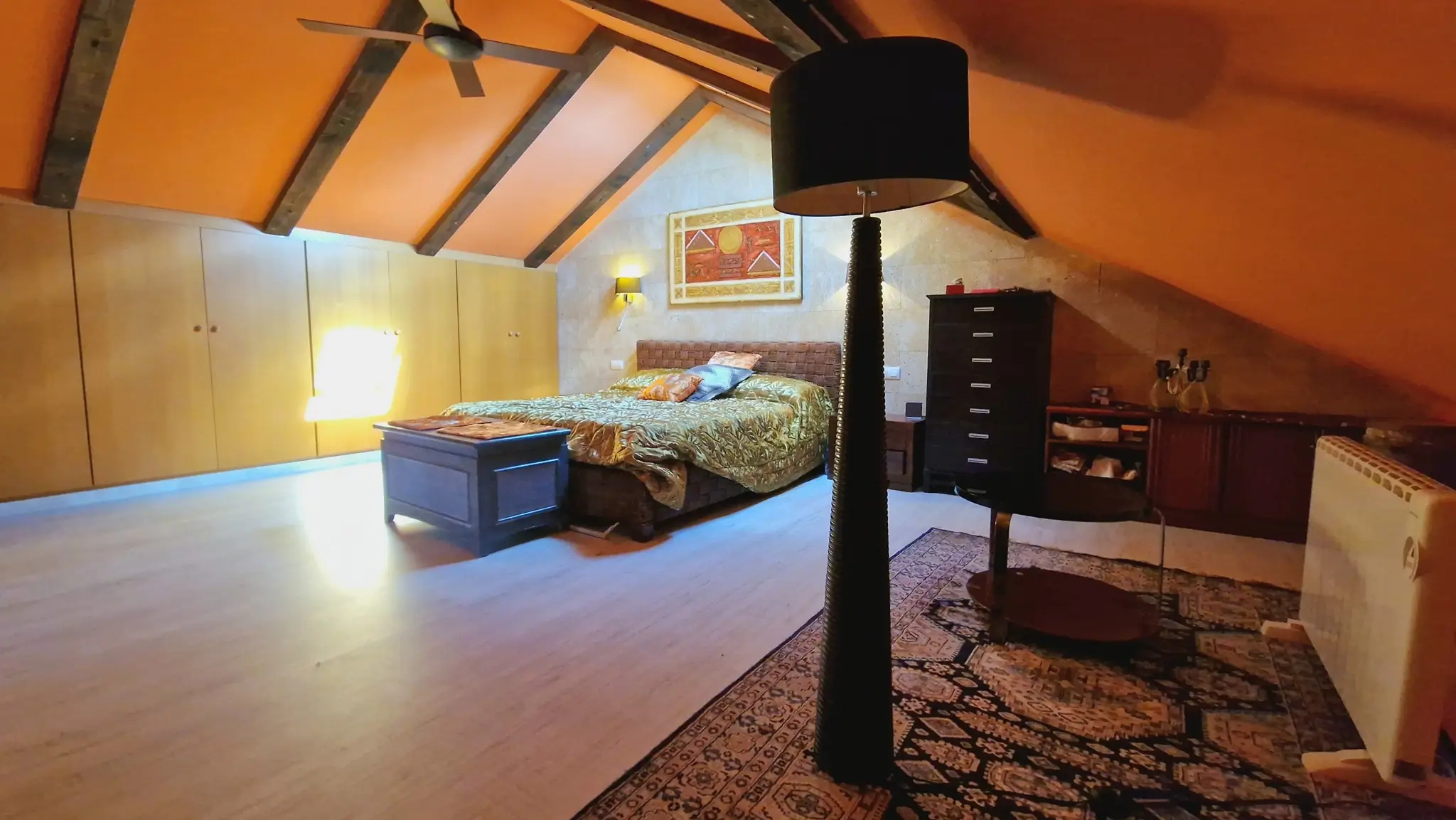 Dachgeschoss-Schlafzimmer mit dunklen Holzbalken, hellen Einbauschränken und einer Natursteinwand unter der charakteristischen Dachschräge.