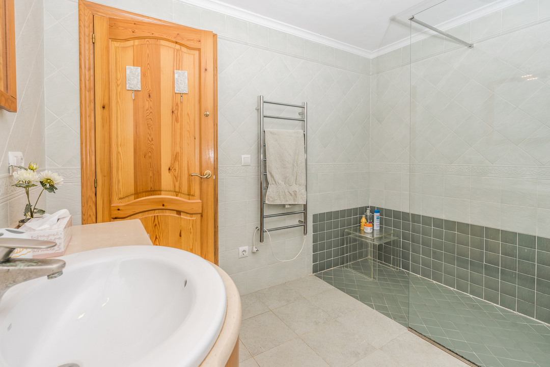 Badezimmer mit begehbarer Dusche, grünen Fliesen, Glastrennwand und verchromtem Handtuchwärmer neben einer massiven Holztür.