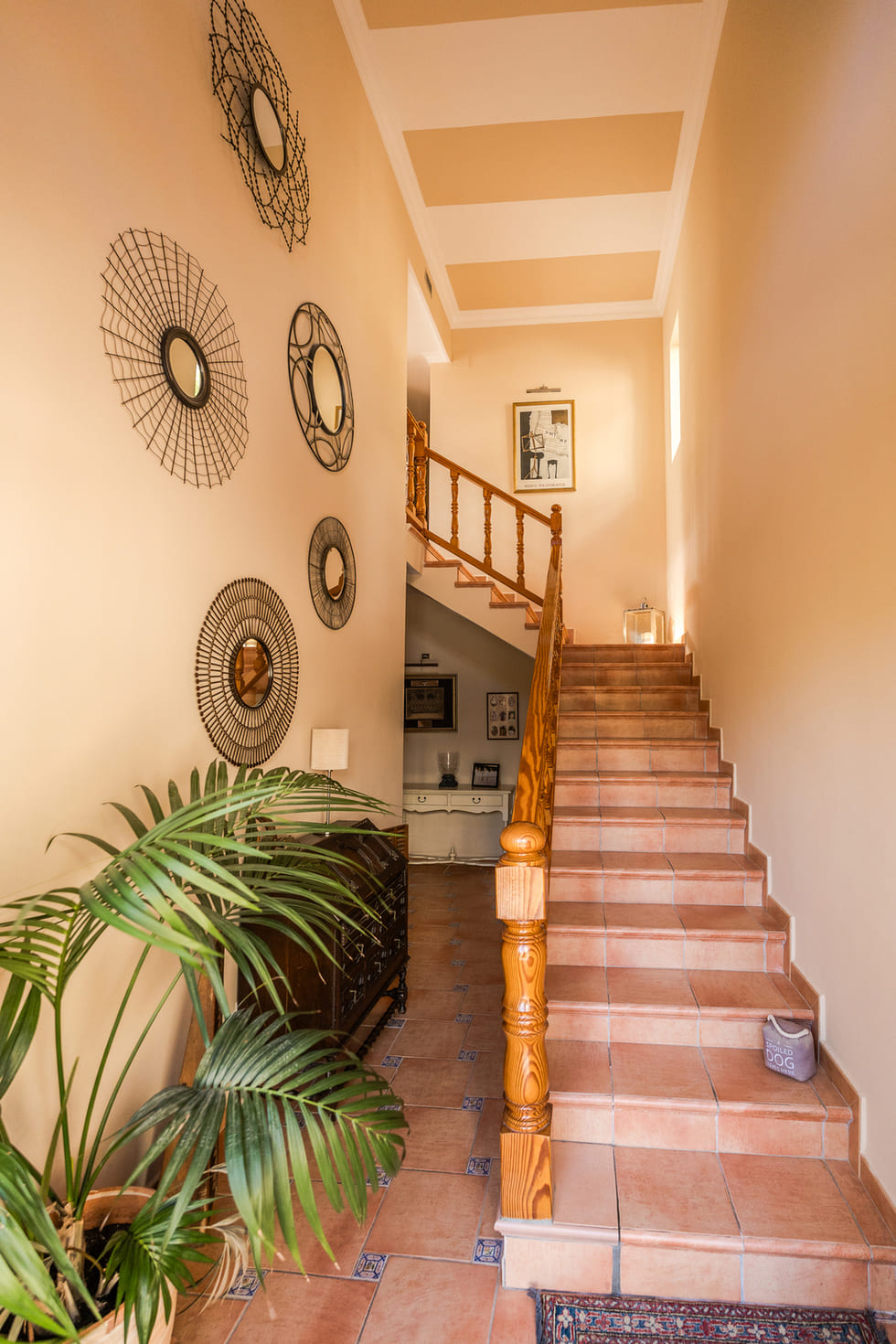 Eingangsbereich mit Terrakotta-Treppe, Holzgeländer, dekorativen Drahtspiegeln an der Wand und einer gestreiften Decke.