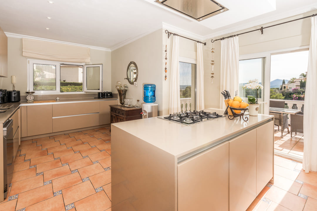 Großzügige Küche mit Kochinsel, Gaskochfeld, beigen Fronten und Terrakottaboden. Große Fenster und der Terrassenzugang sorgen für viel Tageslicht und eine offene Atmosphäre.