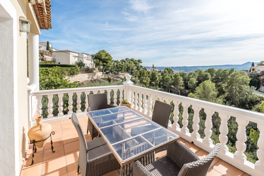 Hochgelegene Terrasse mit Glastisch, Rattanstühlen und weißer Balustrade, die einen weiten Blick über das pinienbewachsene Tal und die Hügel bietet.