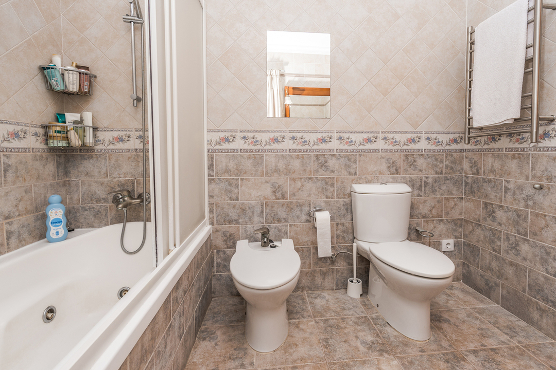 Komplettes Badezimmer mit Badewanne, Bidet und WC. Erdfarbene Wandfliesen mit dekorativer Blumenbordüre und ein Handtuchheizkörper ergänzen die funktionale Ausstattung.