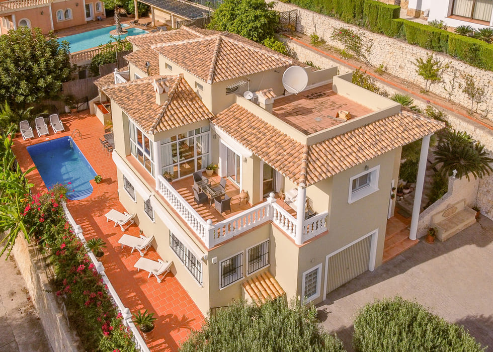 Luftaufnahme einer mediterranen Villa mit Terrakottadächern, privatem Pool und Terrassen mit weißen Balustraden sowie Essbereich im Freien.