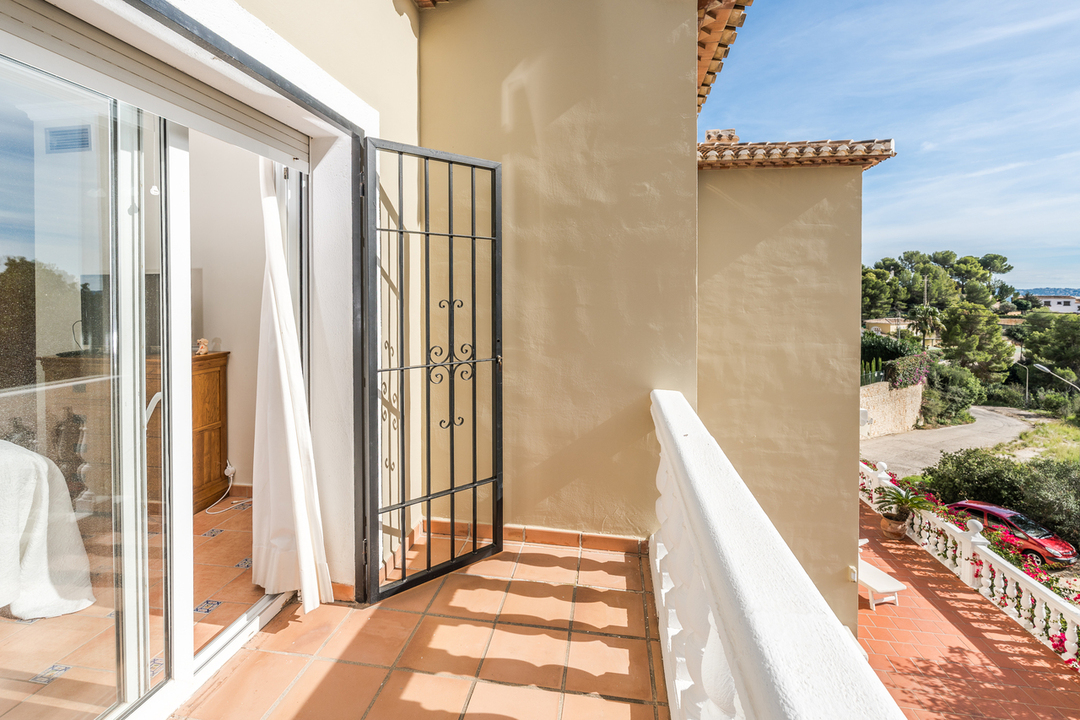 Privater Balkon mit Terrakotta-Fliesen und weißer Balustrade, ausgestattet mit einem schmiedeeisernen Sicherheitsgitter und Blick auf die Umgebung.