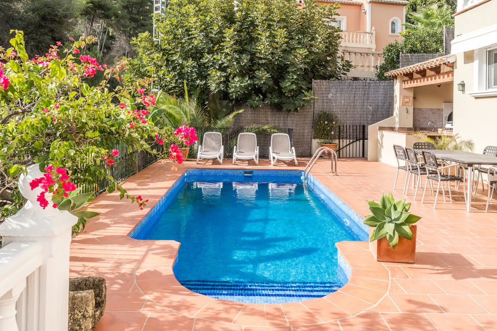 Rechteckiger Pool mit blauen Mosaikfliesen, umgeben von einer Terrakotta-Terrasse, Sonnenliegen und einem Essbereich im Freien mit Bougainvillea.