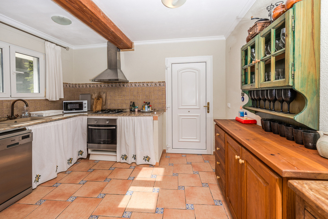 Rustikale Küche mit Terrakottaboden, sichtbaren Holzbalken, Granitarbeitsplatten und einem grünen Hängeschrank aus Holz über dem Sideboard.