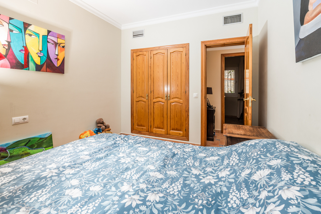 Schlafzimmer mit Einbauschrank aus Holz, hellen Wänden mit moderner Kunst und einem Bett mit blau-weißer floraler Bettwäsche.