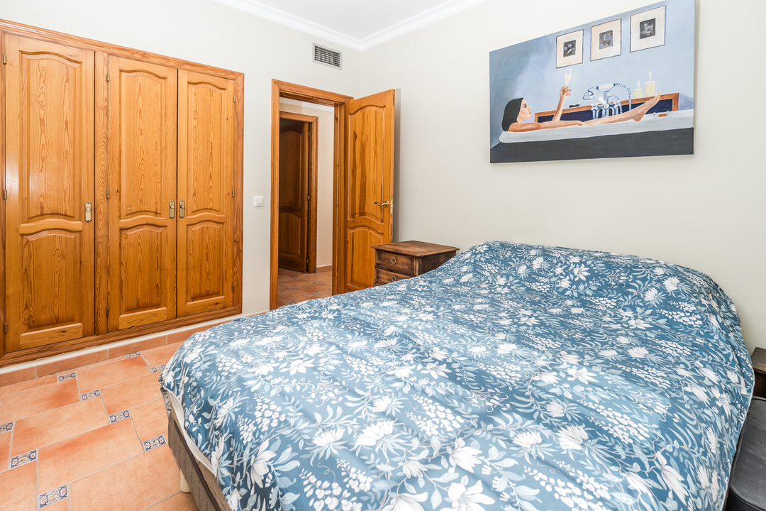 Schlafzimmer mit Einbauschrank aus Naturholz, Terrakottaboden mit blauen Akzenten und Doppelbett mit floralem Textildesign.