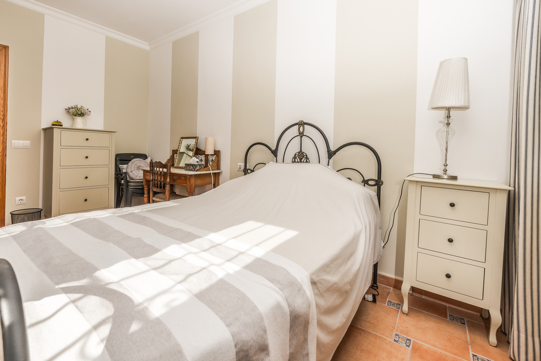Schlafzimmer mit schmiedeeisernem Kopfteil, gestreifter Tapete und Terrakottaboden. Mit cremefarbener Nachtkonsole und klassischem Holz-Schminktisch.