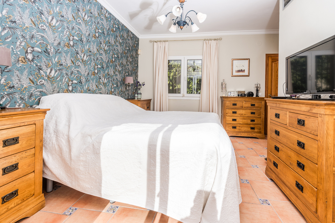 Schlafzimmer mit tropischer Mustertapete, passenden Holzkommoden und Terrakotta-Fliesenboden mit dekorativen blauen Einlegern.