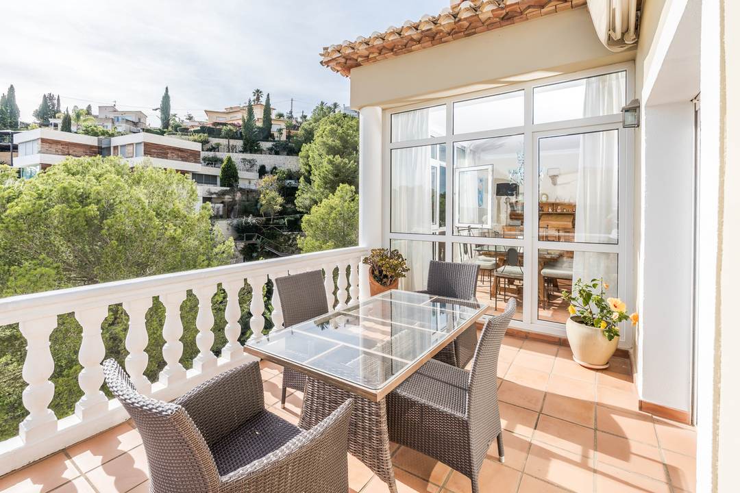 Terrasse mit Terrakotta-Fliesen, weißer Balustrade und einem Esstisch aus Glas. Sie bietet Ausblick auf die bewaldete Hügellandschaft und benachbarte Villen.