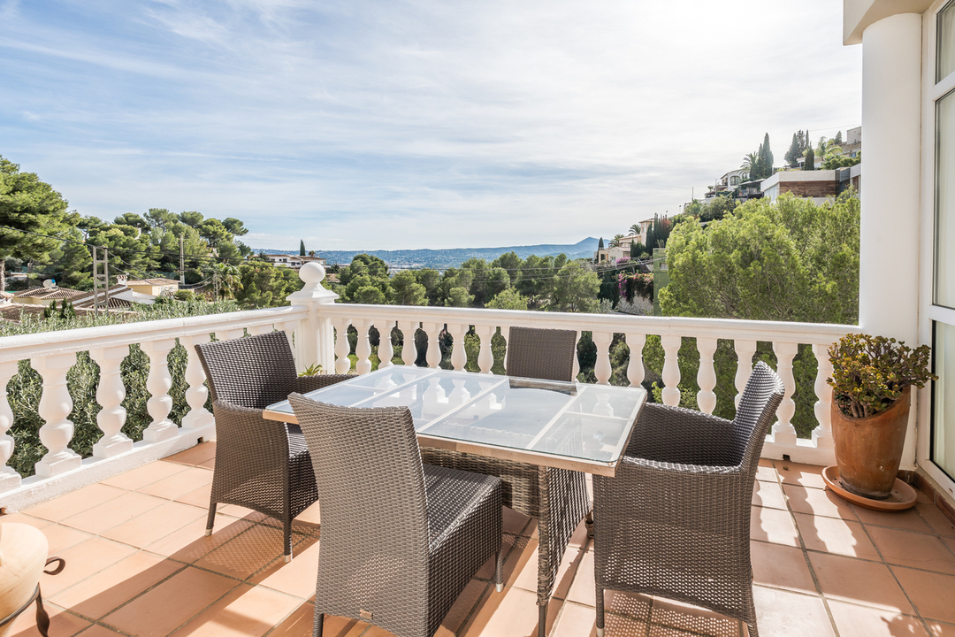 Terrasse mit Terrakottafliesen und weißer Balustrade, ausgestattet mit einer Korbsitzgruppe und Panoramablick auf das Tal und die Berge.