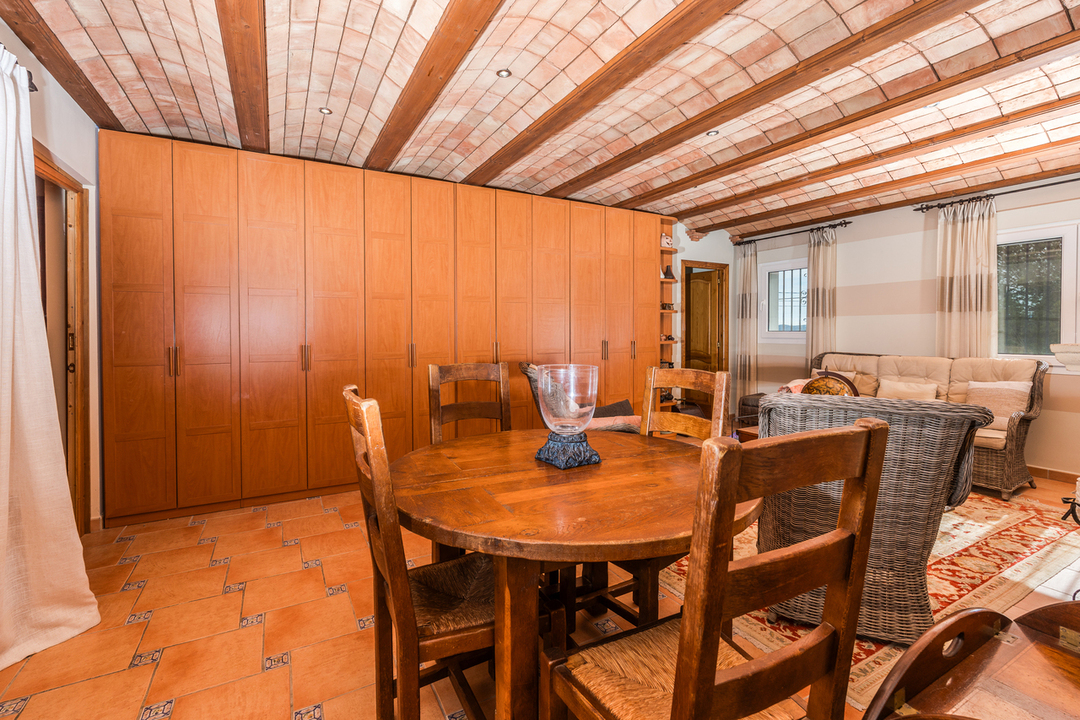 Wohnbereich mit katalanischem Gewölbe, Holzbalken, rustikalen Terrakottafliesen und einer großzügigen Einbauschrankwand aus Holz.