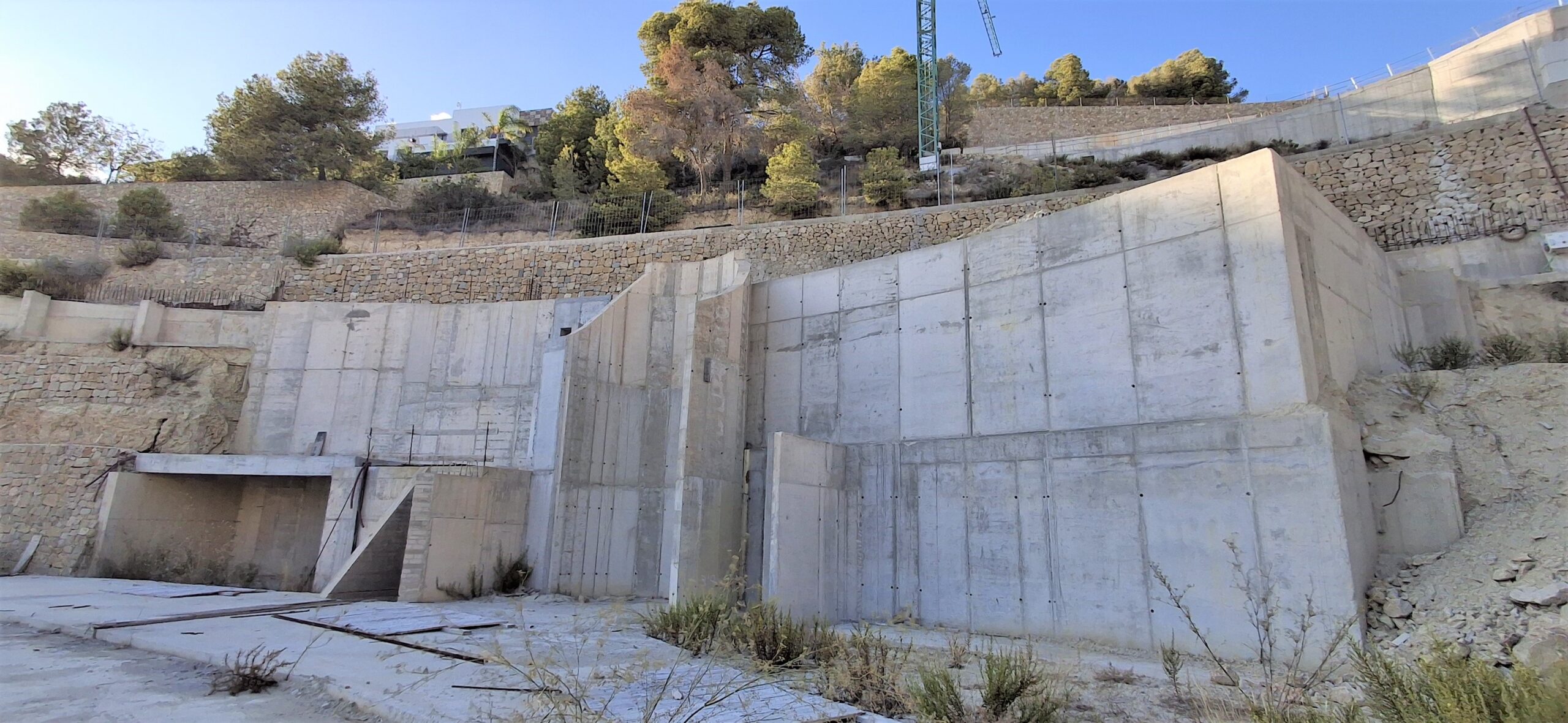 Ansicht der Stahlbeton-Stützwände und Steinterrassen, die in ein steiles Hanggrundstück mit mediterraner Vegetation integriert sind.