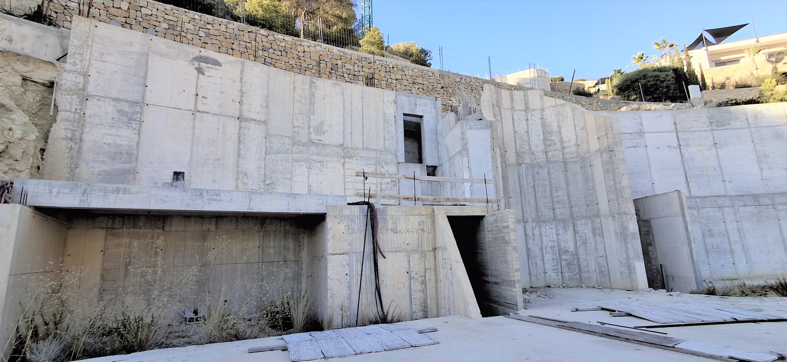 Strukturansicht der Stahlbeton-Stützmauern mit integriertem Steinmauerwerk auf der oberen Ebene und architektonischen Öffnungen in Hanglage.