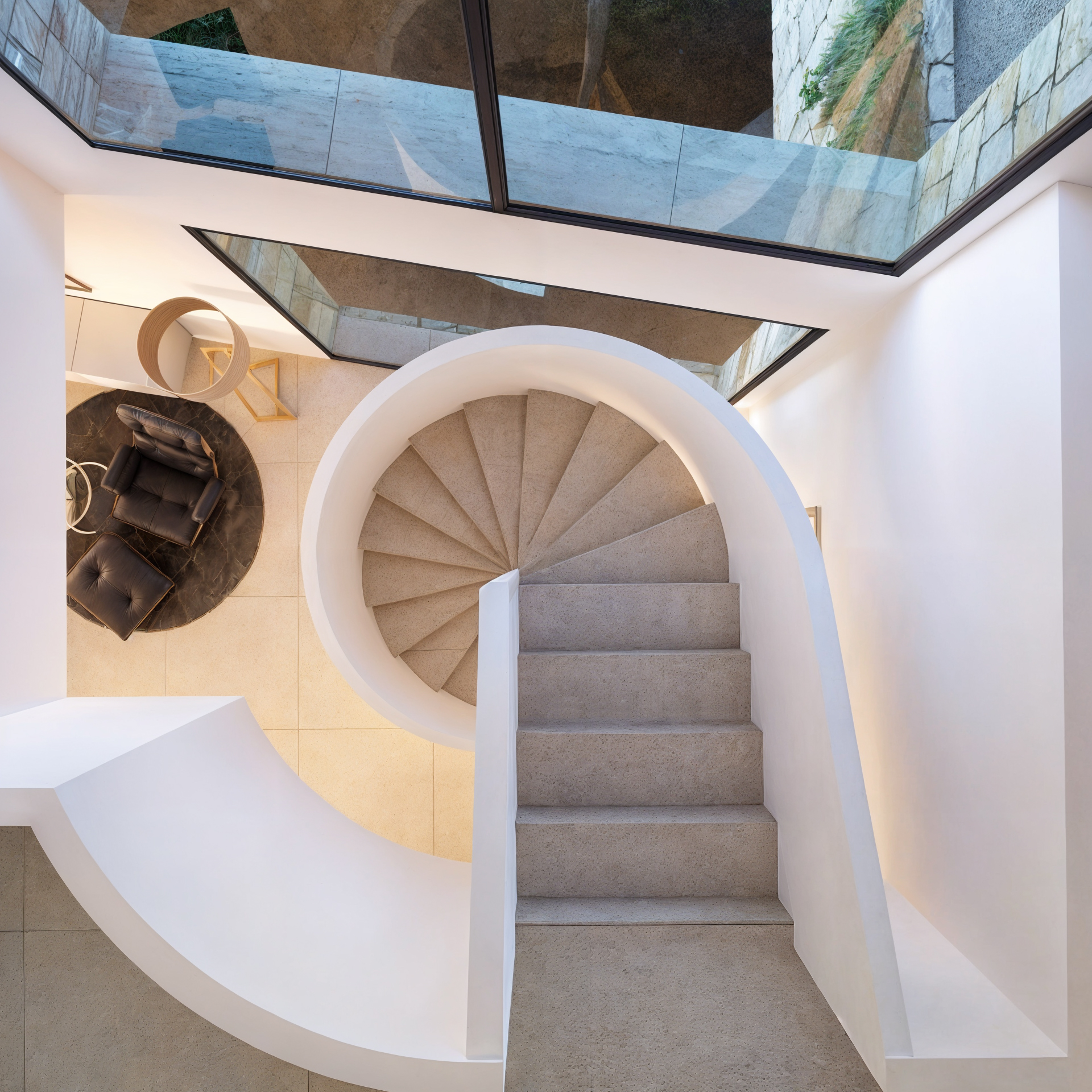 Wendeltreppe aus Stein mit weißen geschwungenen Brüstungen aus der Vogelperspektive, mit großen Glasflächen und einem Loungebereich darunter.
