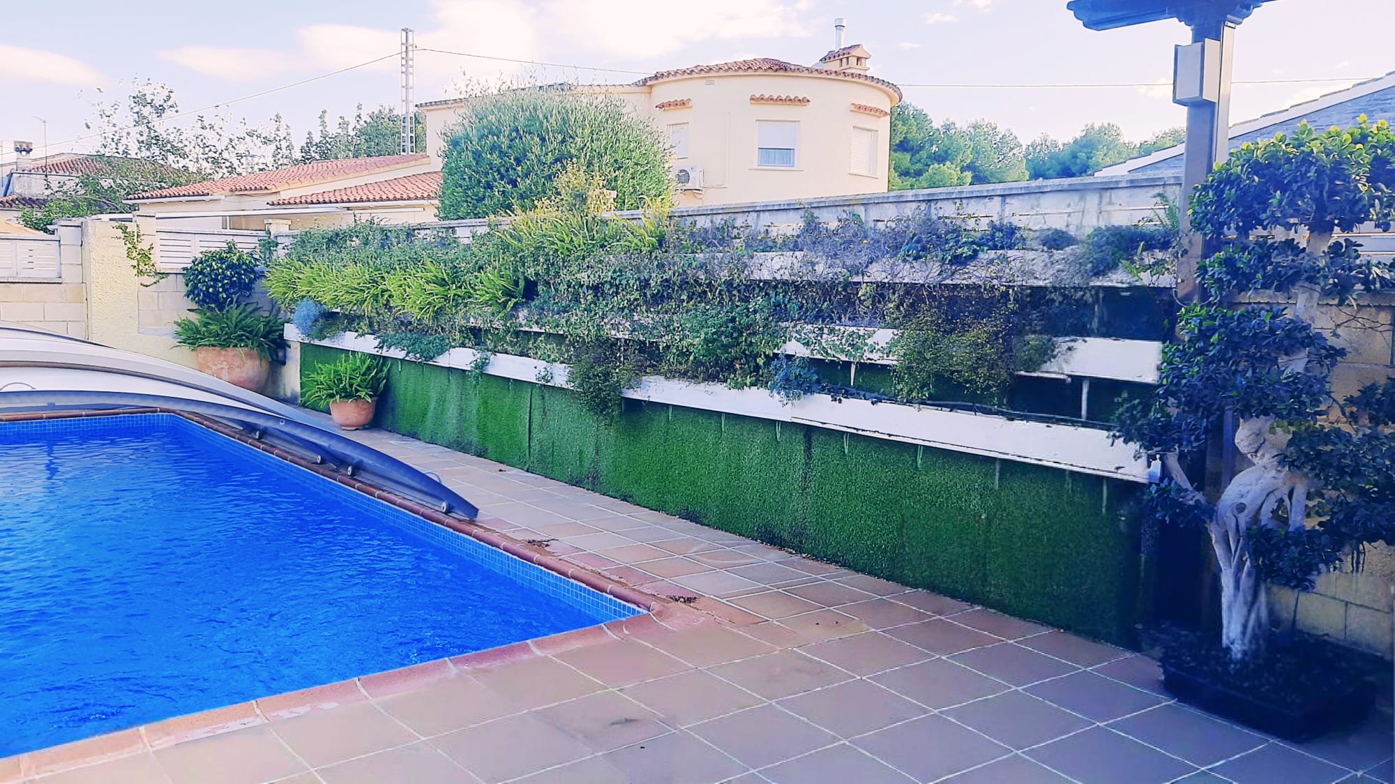 Außenpoolbereich mit gefliester Terrasse, einziehbarer Poolabdeckung und einer mehrstufigen vertikalen Gartenwand auf Kunstrasenbasis.