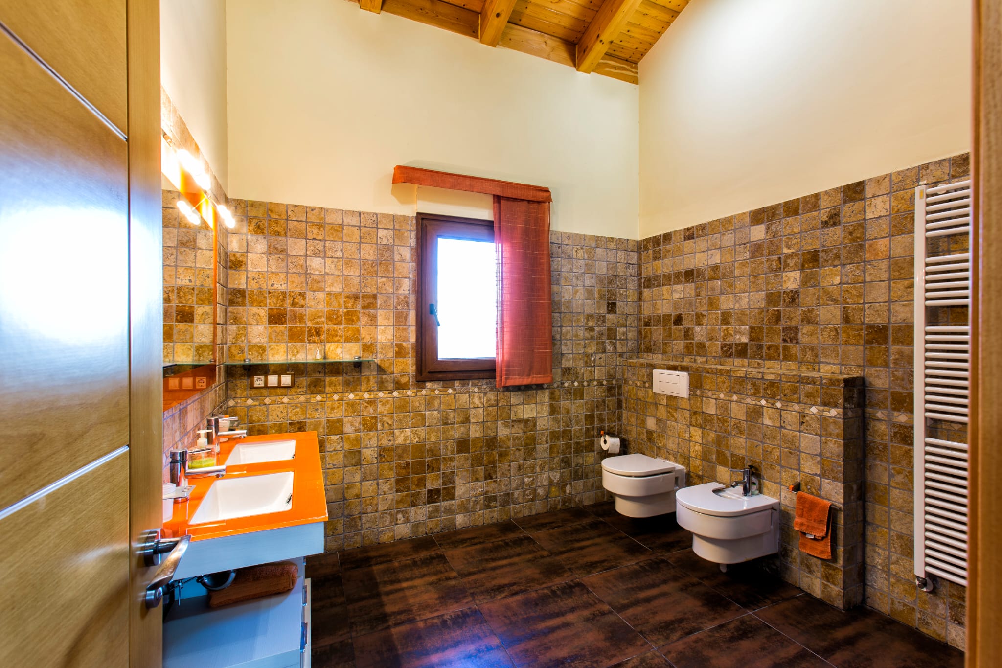 Modernes Badezimmer mit Doppelwaschtisch in Orange, Natursteinwänden und einer gewölbten Holzdecke mit sichtbaren Balken.