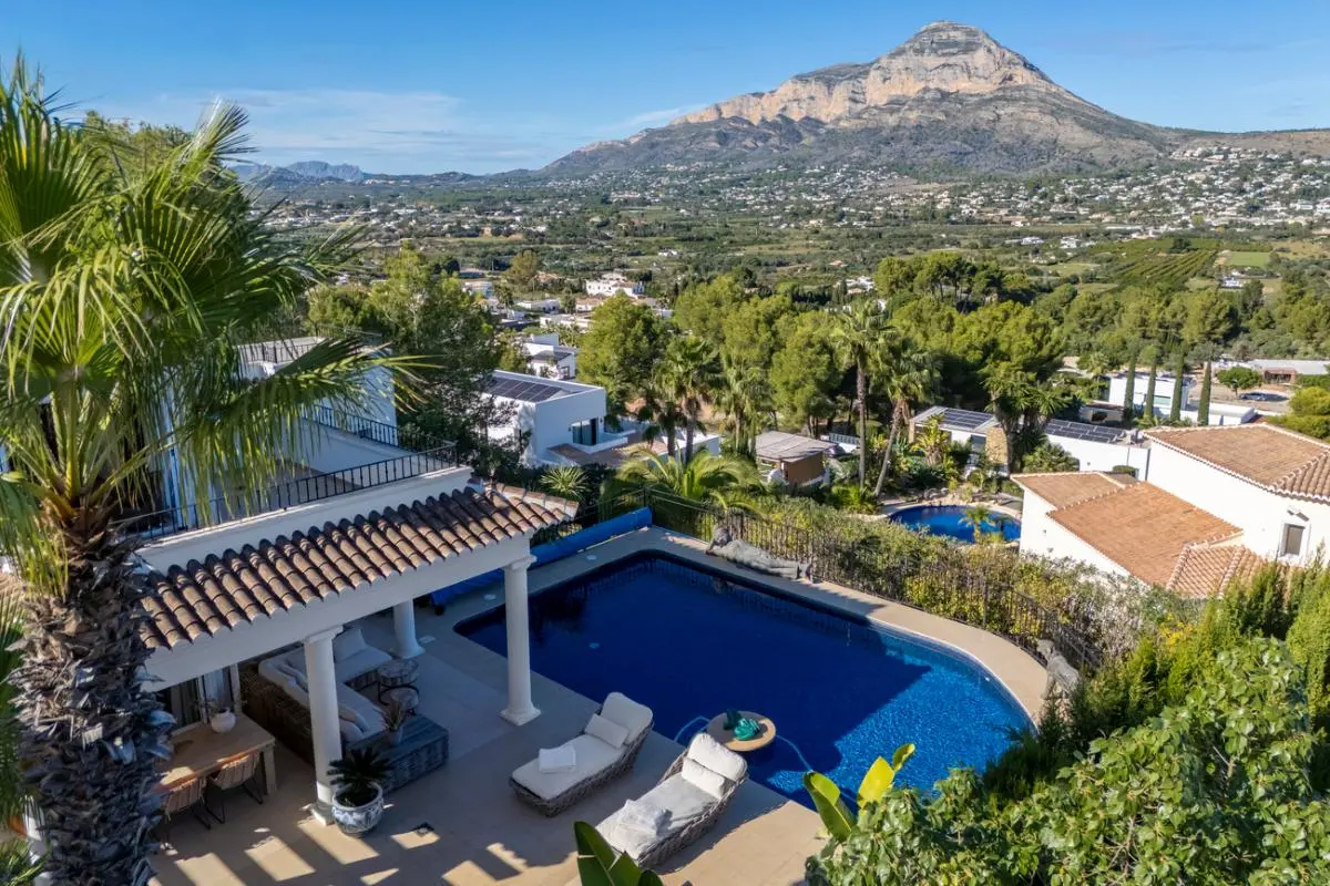 Erhöhte Ansicht des privaten Pools und der überdachten Terrasse mit weißen Säulen, mit weitem Blick über das Tal und das Montgó-Massiv.