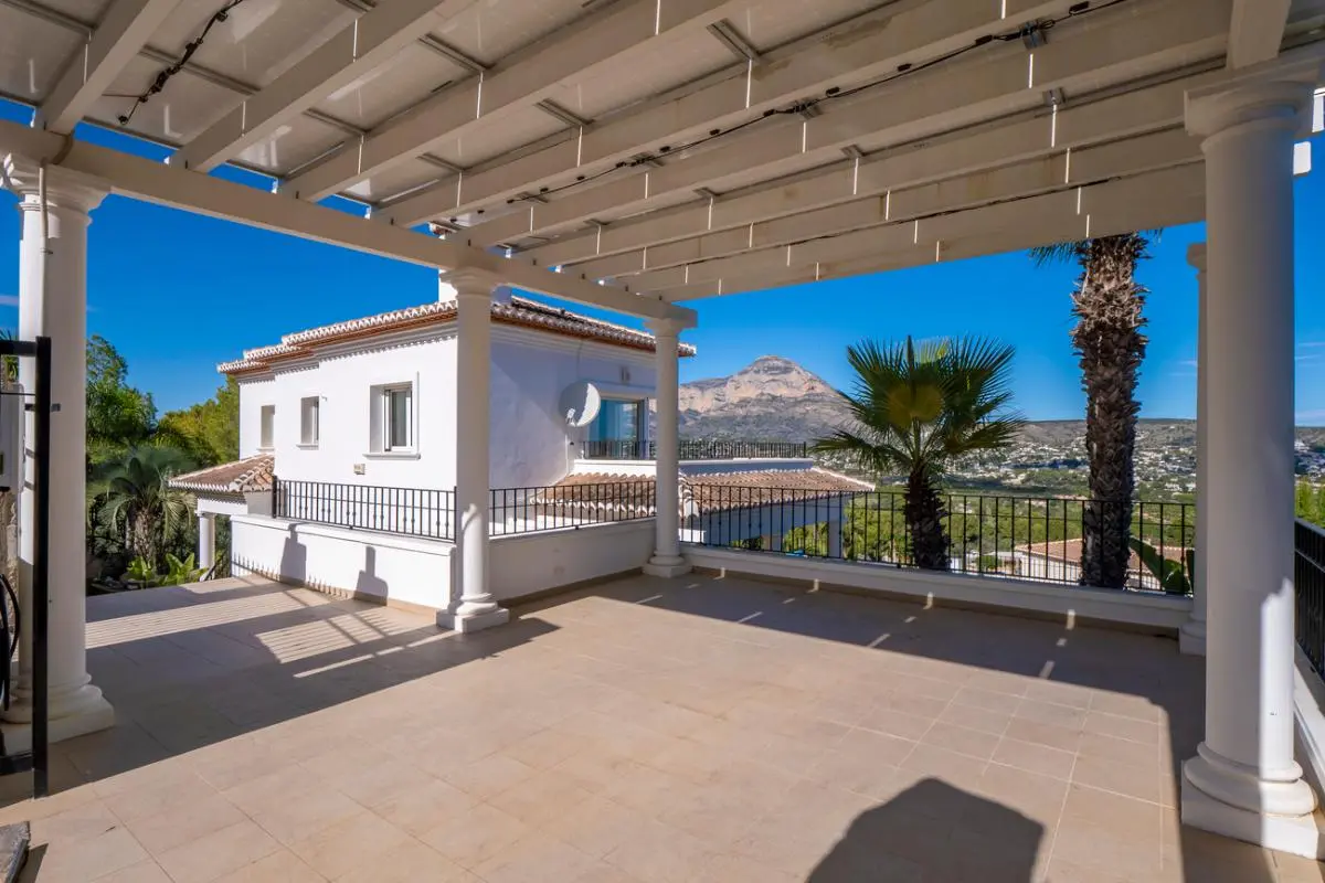 Großzügige überdachte Terrasse mit weißen Säulen und Pergola, die einen weiten Blick auf den Berg Montgó und die mediterrane Landschaft bietet.