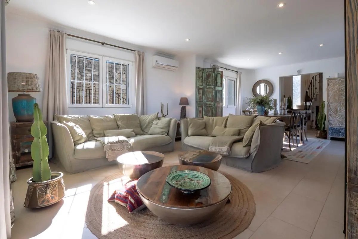 Großzügiges Wohnzimmer mit neutralen Sofas, runden Holztischen auf einem Juteteppich und rustikalem Dekor bei natürlichem Lichteinfall.