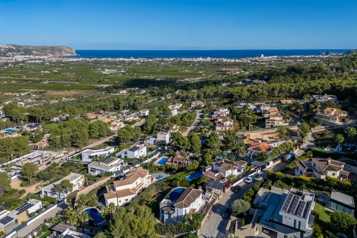 Luftbild eines Wohnviertels in Hanglage mit Villen, privaten Pools und Solarmodulen, mit weitem Blick über das Tal bis hin zur Mittelmeerküste.
