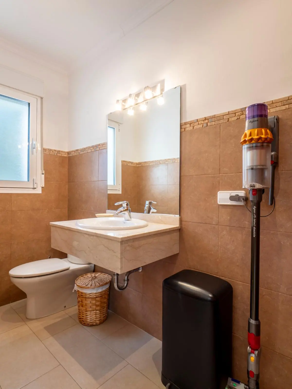 Modernes Badezimmer mit schwebendem Marmorwaschtisch, beigen Wandfliesen und integriertem Waschbecken. Inklusive Wandhalterung für Staubsauger und Tageslicht.