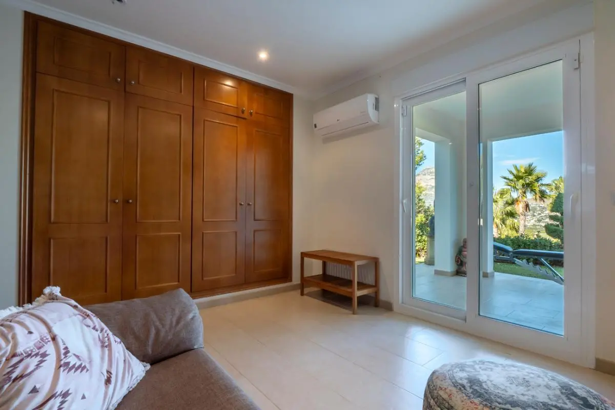 Schlafzimmer mit großem Einbauschrank aus Holz, Klimaanlage und Glasschiebetüren mit direktem Zugang zur Terrasse und Blick in den Garten.