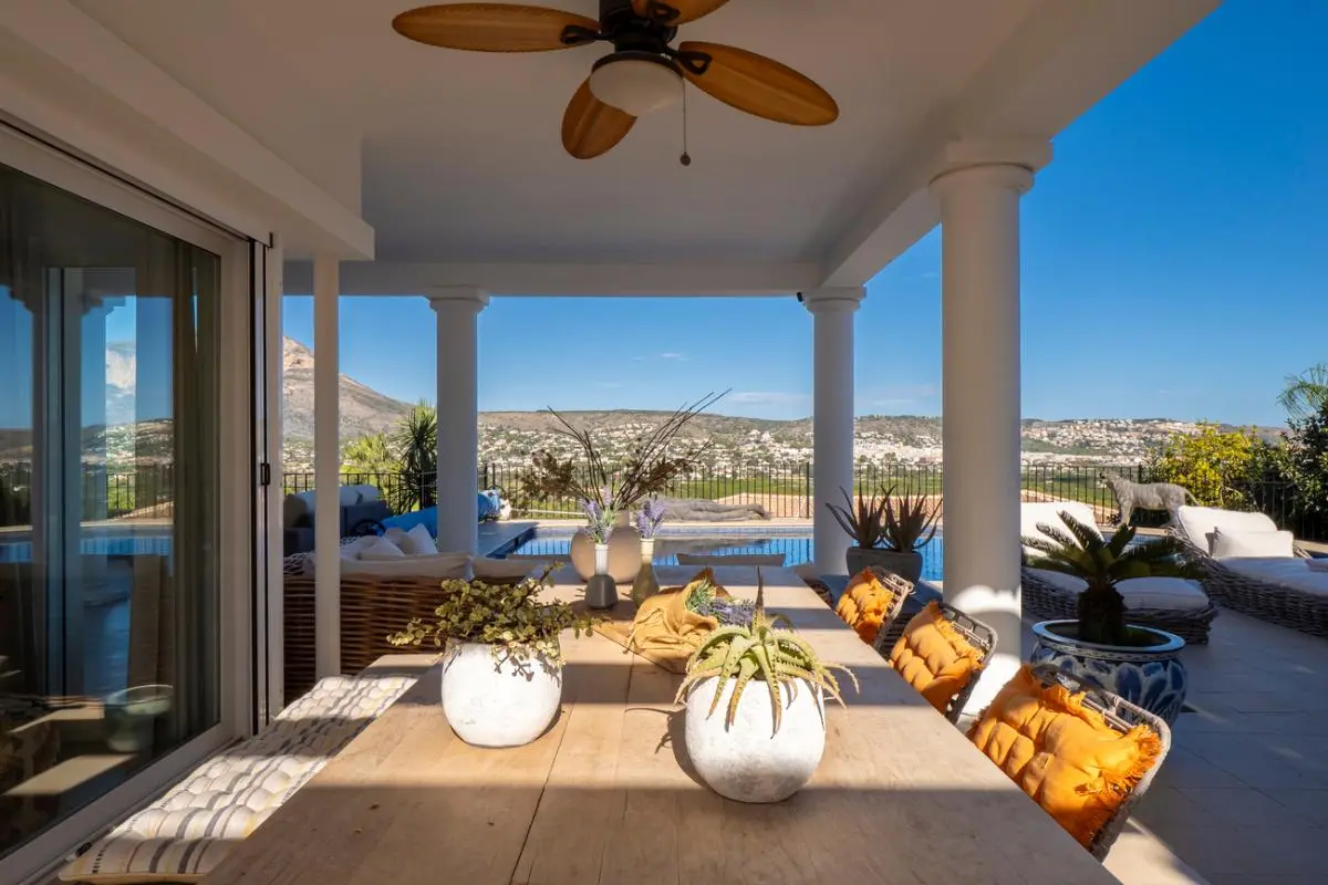 Überdachte Terrasse mit Holzesstisch, Deckenventilator und Panoramablick auf den Pool und die umliegende Berglandschaft.