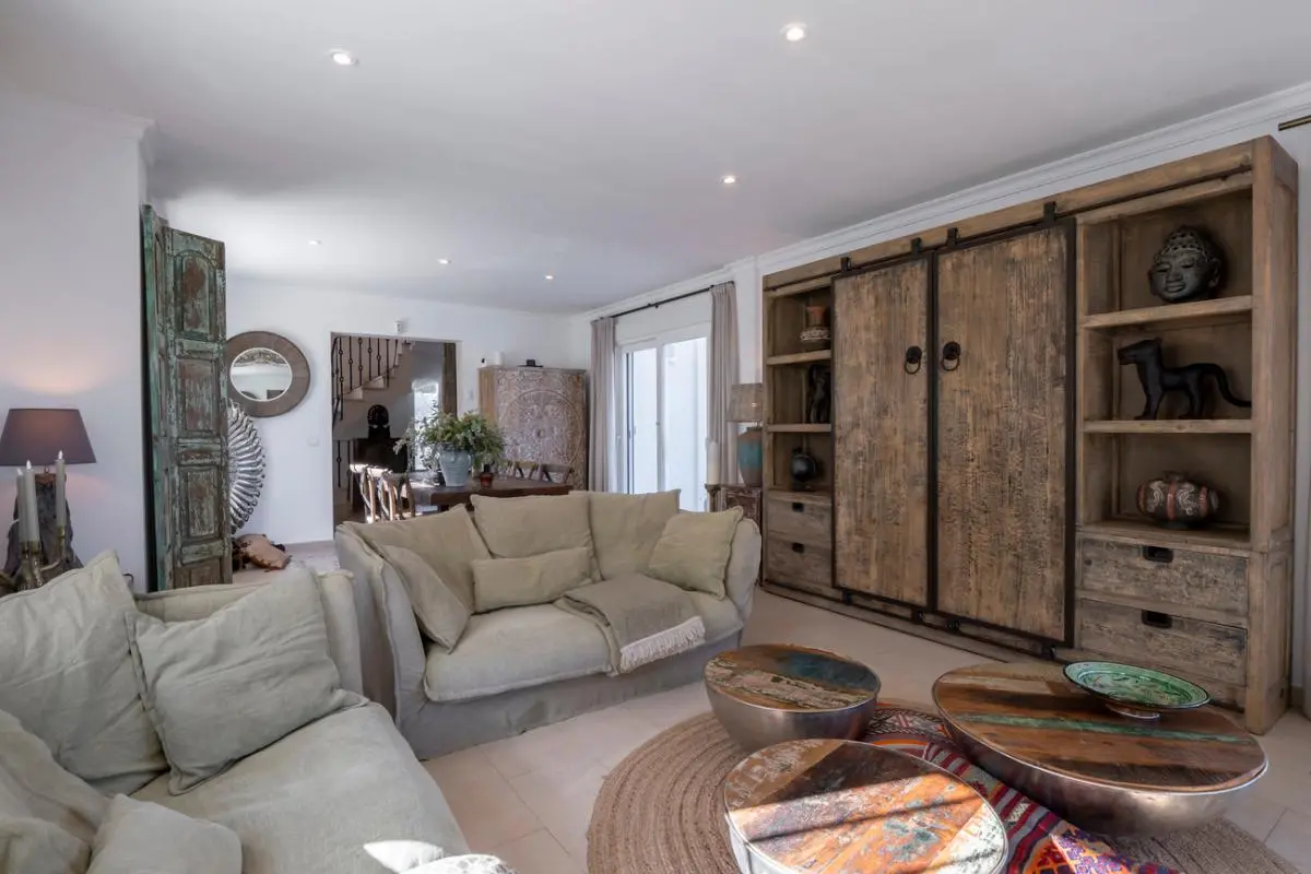 Wohnbereich mit einer großen rustikalen Holzwand, beigen Leinensofas und runden Couchtischen aus Altholz auf einem kreisförmigen Jute-Teppich.
