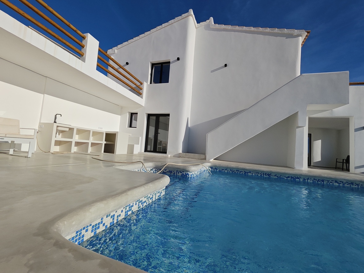 Außenbereich mit blau gefliestem Pool, integrierter Außenküche und minimalistischer weißer Fassade mit Holzgeländern und Außentreppe.