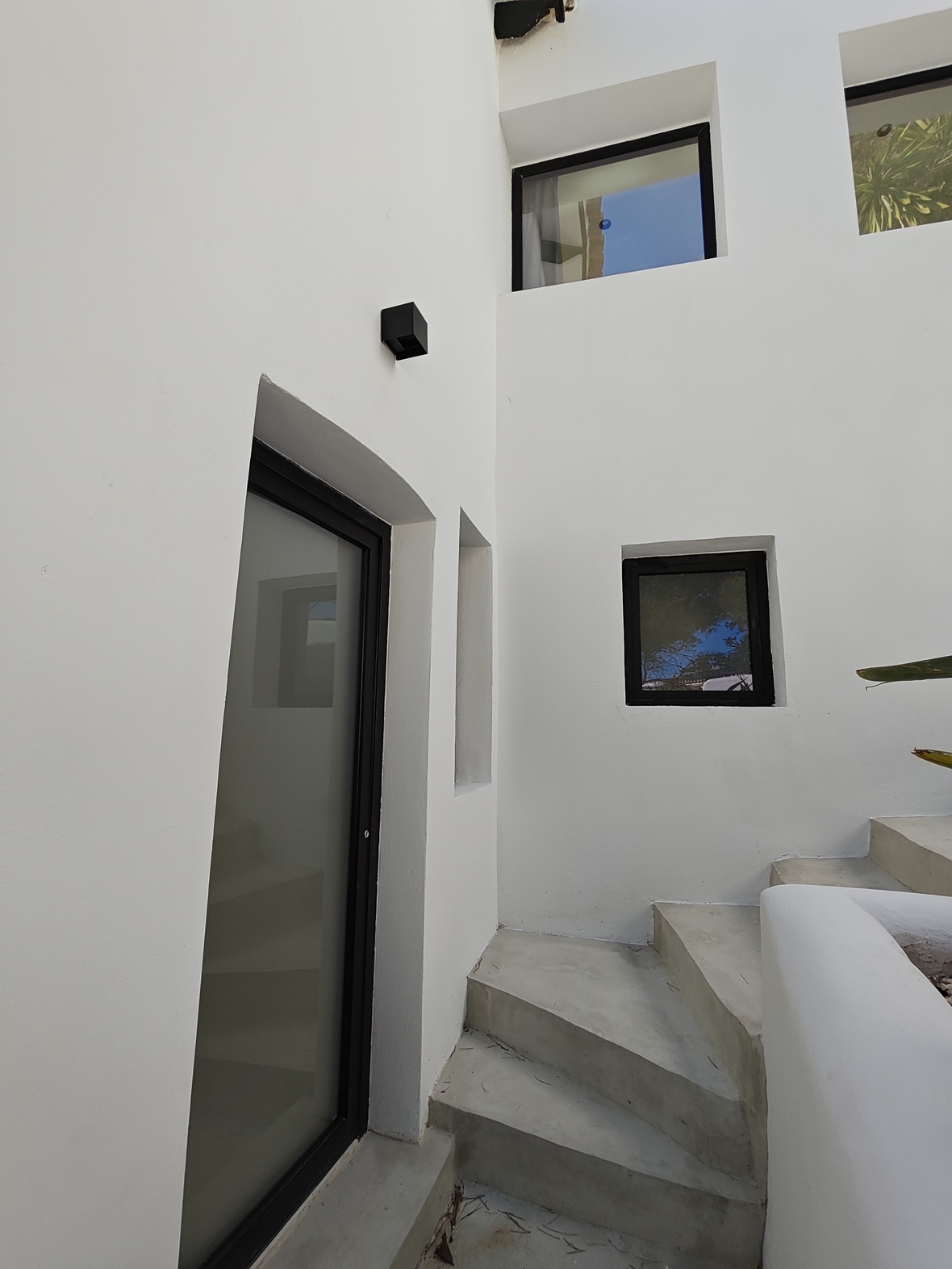 Außenliegende Betontreppe an minimalistischen weißen Wänden mit schwarz gerahmten Fenstern und einer matten Glastür.