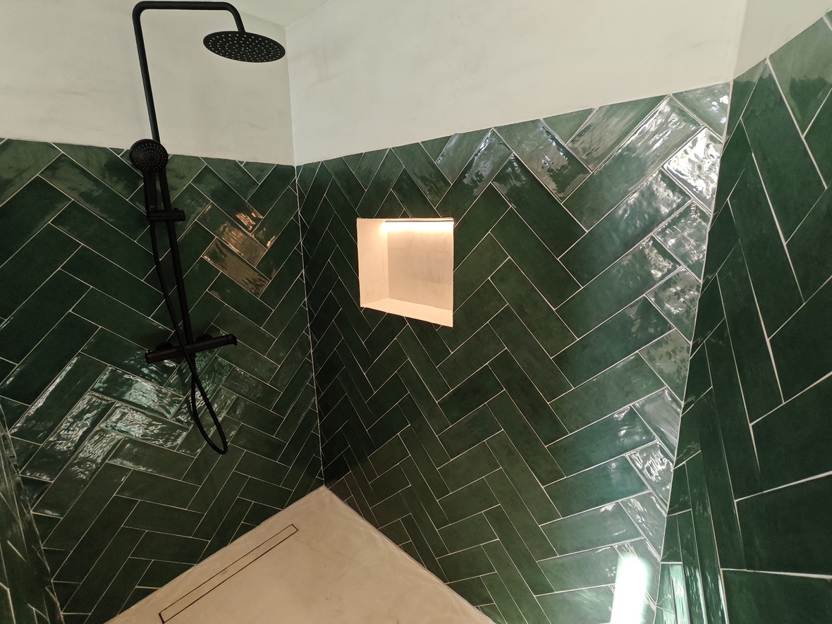 Dusche mit smaragdgrünen Fischgrätfliesen, mattschwarzen Armaturen und einer beleuchteten Wandnische. Heller Boden mit integrierter Linienentwässerung.