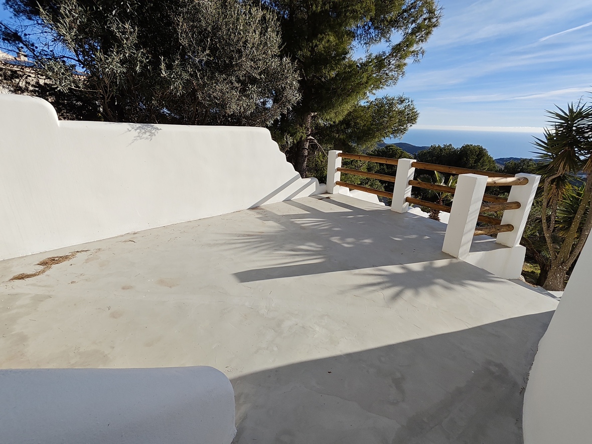 Erhöhte Terrasse mit glattem Betonboden, weiß verputzten Mauern und Holzgeländer mit Panoramablick auf das Mittelmeer und den angrenzenden Pinienwald.