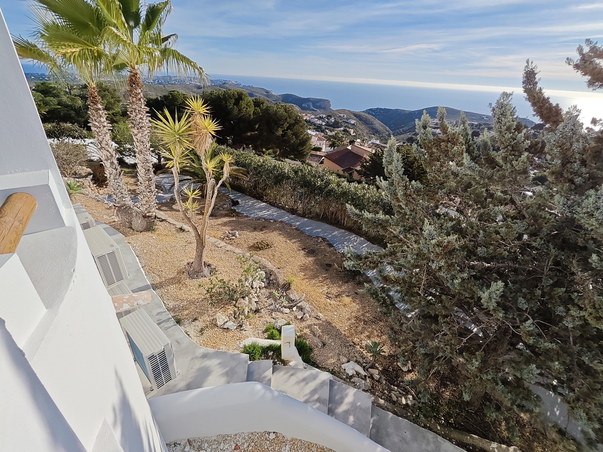 Erhöhter Blick auf einen Garten mit Palmen und Kieswegen, der eine Panorama-Aussicht über das Küstental bis hin zum Mittelmeer bietet.