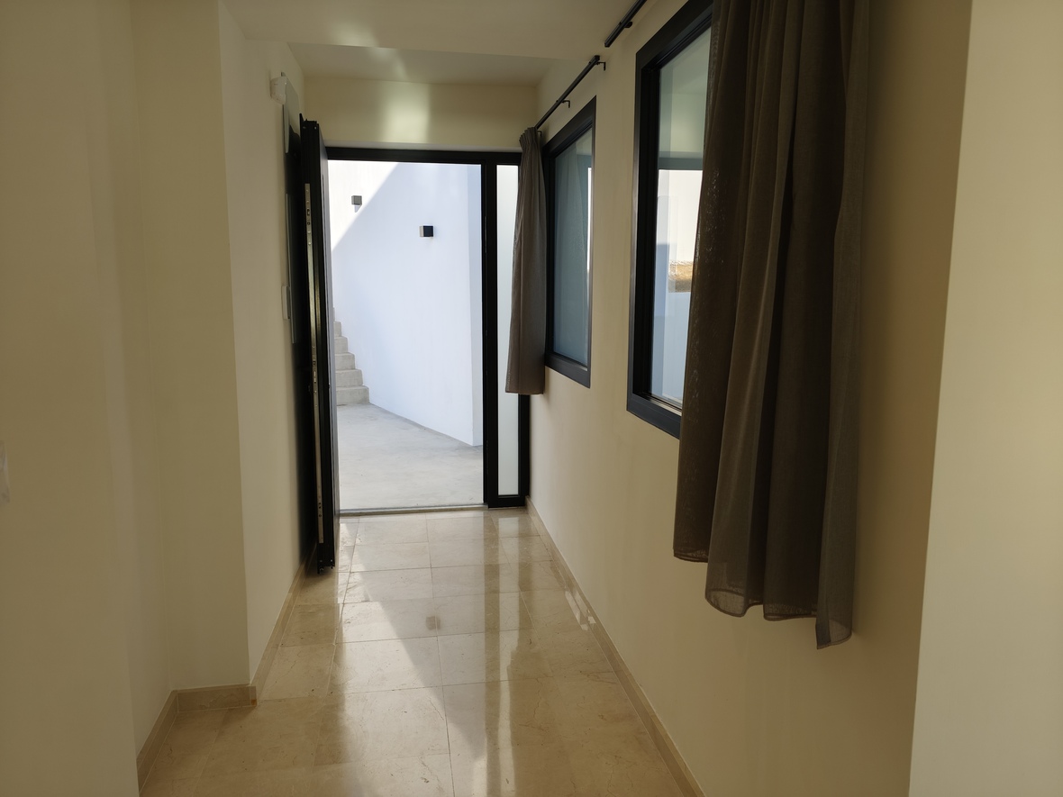 Flur mit poliertem Marmorboden und Zugang zu einem Innenhof mit Steintreppe. Ausgestattet mit schwarzen Fensterrahmen und neutralen Vorhängen.