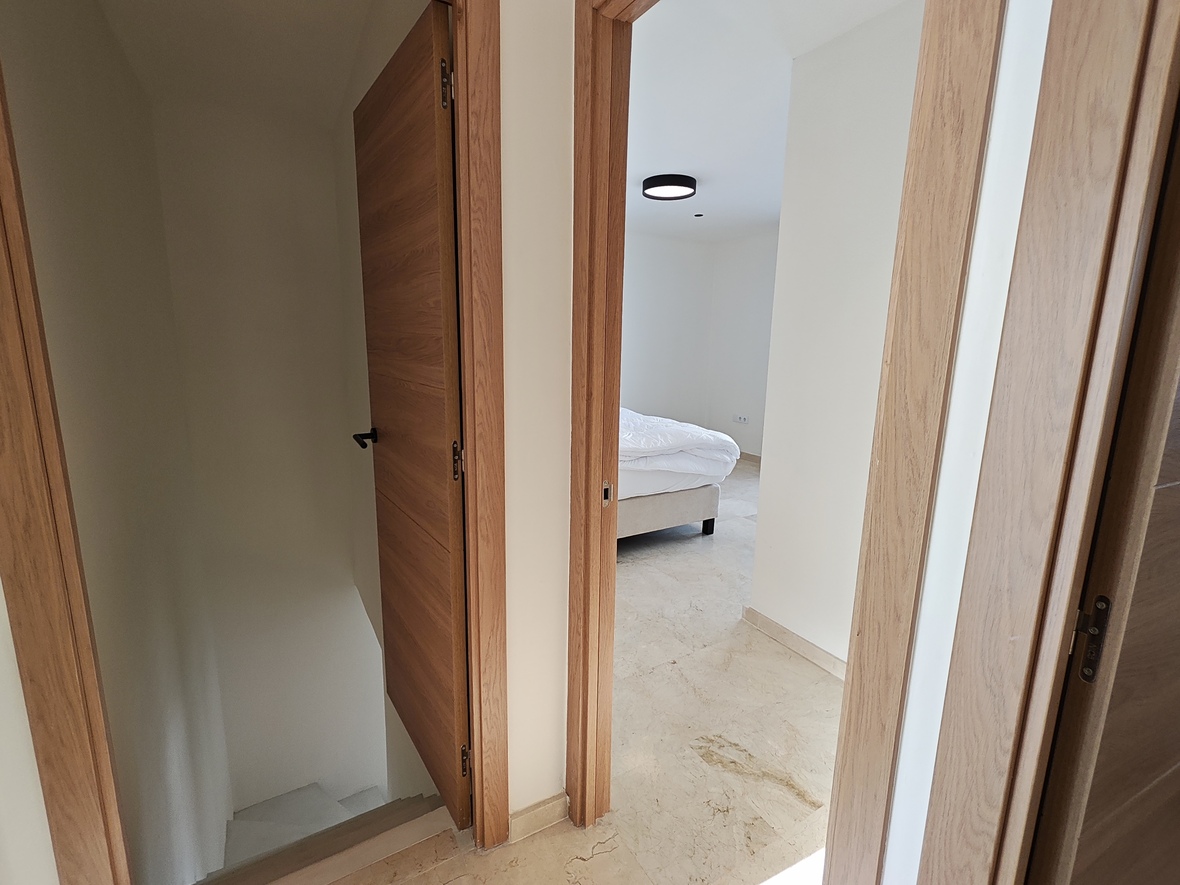 Flurbereich mit Eichentüren und Natursteinboden, der den Zugang zu einem Schlafzimmer und der Treppe ins Untergeschoss verbindet.