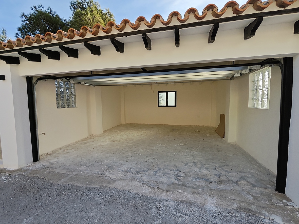 Geräumige Garage mit Betonboden, Glasbausteinfenstern für natürliches Licht und traditionellem Ziegeldach mit dunklen Holzbalken.