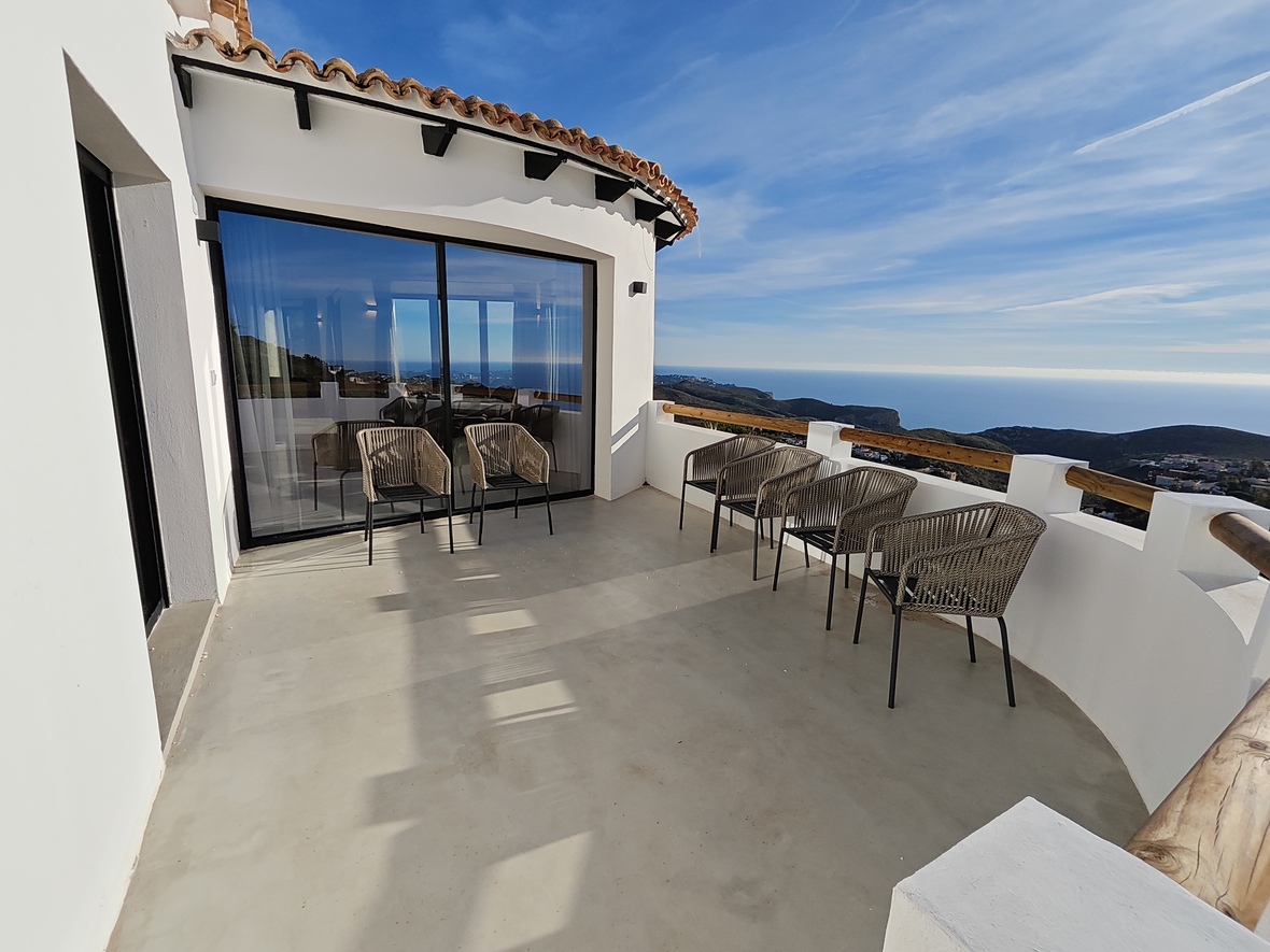 Großzügige, geschwungene Terrasse mit Mikrozementboden, geflochtenen Sesseln und Panoramablick auf das Mittelmeer vor einer weißen Fassade.