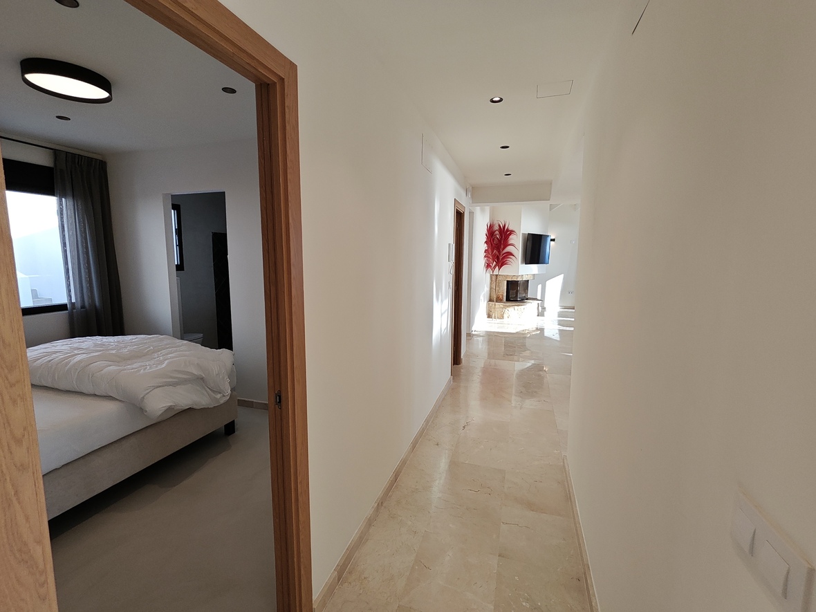 Heller Flur mit poliertem Marmorboden, der zu einem Wohnbereich mit Steinkamin führt, inklusive Blick in ein Schlafzimmer mit Holzrahmen.