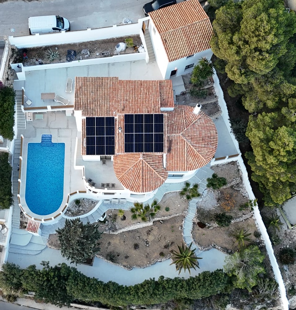 Luftaufnahme einer mediterranen Villa mit Solarmodulen auf dem Ziegeldach, geschwungenem Pool und terrassierten Gärten mit einheimischer Bepflanzung.