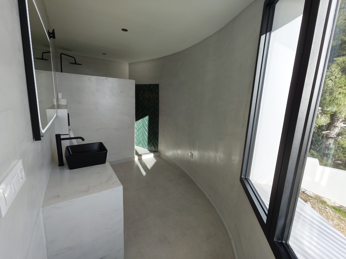 Minimalistisches Badezimmer mit geschwungenen Mikrozementwänden, schwarzem Aufsatzwaschbecken und Dusche mit grünen Fischgrätenfliesen.