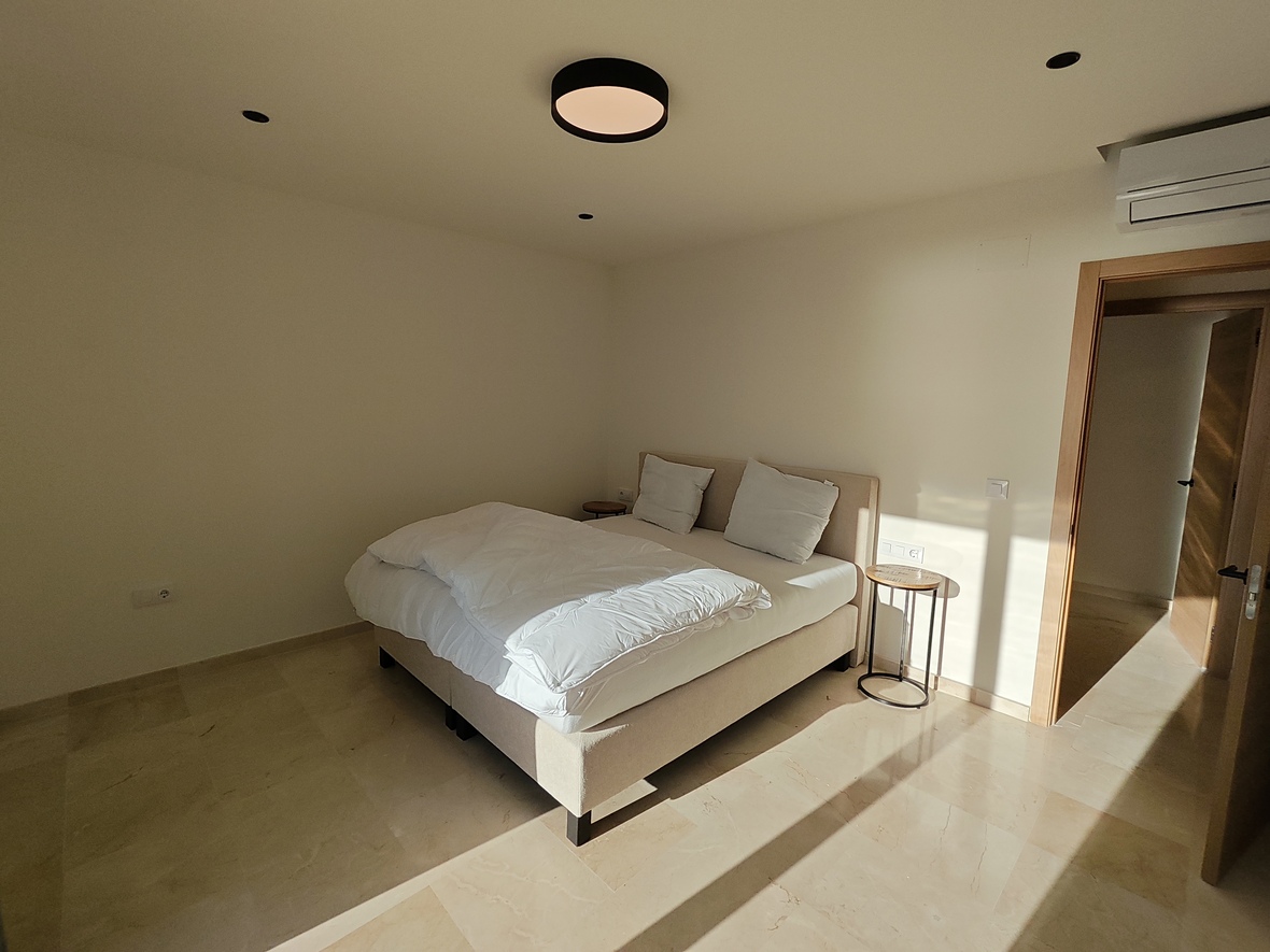 Minimalistisches Schlafzimmer mit poliertem Steinboden, gepolstertem Doppelbett und moderner Beleuchtung inklusive runder Deckenleuchte und Einbaustrahlern.