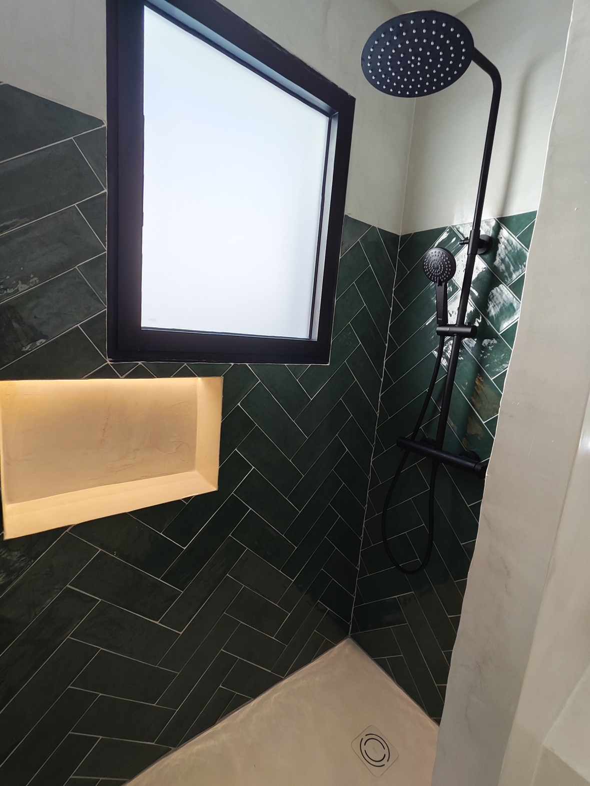 Moderne Dusche mit dunkelgrünen Fischgrätenfliesen, mattschwarzen Armaturen, einer beleuchteten Wandnische und einem Sichtschutzfenster für Tageslicht.