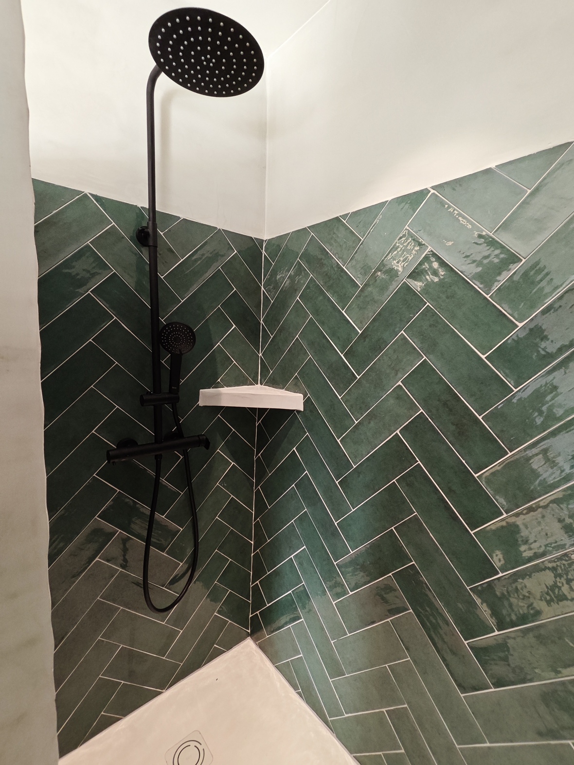 Moderne Dusche mit smaragdgrünen Fliesen im Fischgrätenmuster, mattschwarzen Armaturen und einem großzügigen Regenduschkopf.