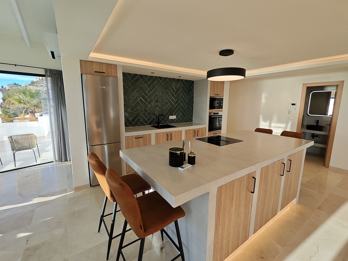 Moderne Küche mit Kochinsel, Steinarbeitsplatte, Lederhockern und grünem Fliesenspiegel im Fischgrätmuster. Integrierte Geräte und direkter Zugang zur Terrasse.
