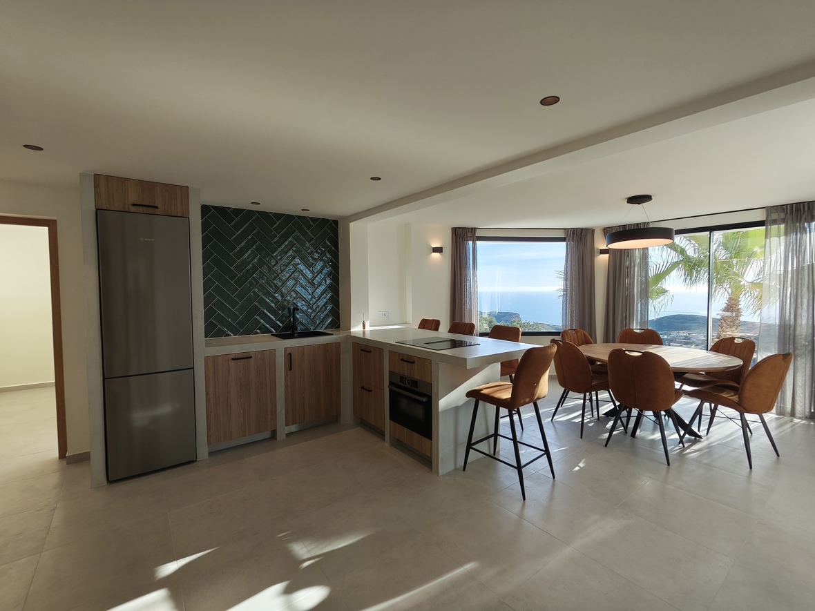 Moderne offene Küche mit grünem Fliesenspiegel im Fischgrätenmuster, integrierten Geräten und Essbereich mit weitem Meerblick durch große Fenster.