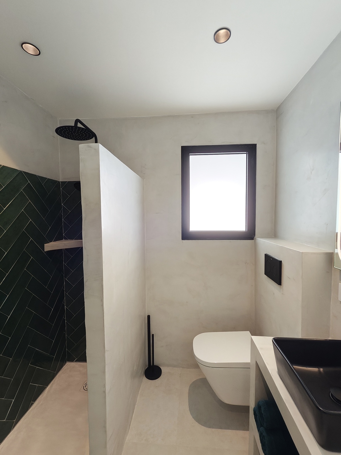 Modernes Badezimmer mit begehbarer Dusche aus grünen Fischgrätfliesen, Wand-WC und weißen Mikrozementwänden mit schwarzen Akzenten.