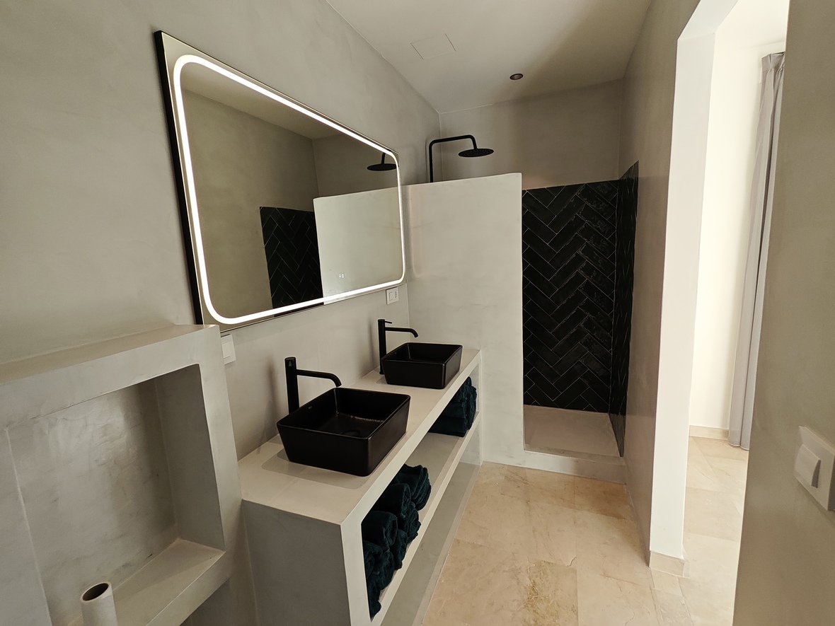 Modernes Badezimmer mit Doppelwaschtisch aus Mikrozement, schwarzen Aufsatzbecken, hinterleuchtetem Spiegel und Dusche mit schwarzen Fischgrätfliesen.
